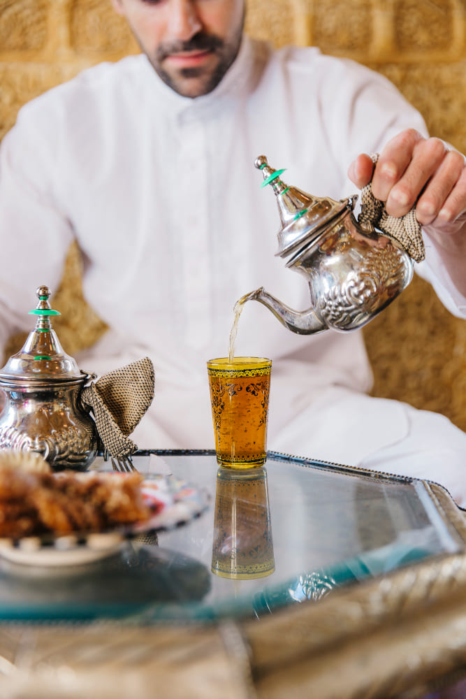 un homme arabe se servant du thé à la menthe dans un verre orné de motifs orientaux
